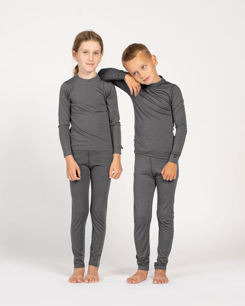 Girl and boy in matching gray Merino wool base layer sets standing side by side, studio background.