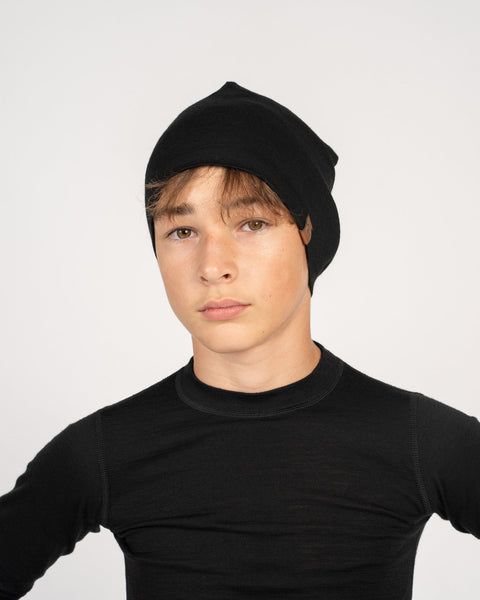 A boy, wearing the menique kids' merino beanie in the color black, dressed n a black long sleeve top as well.