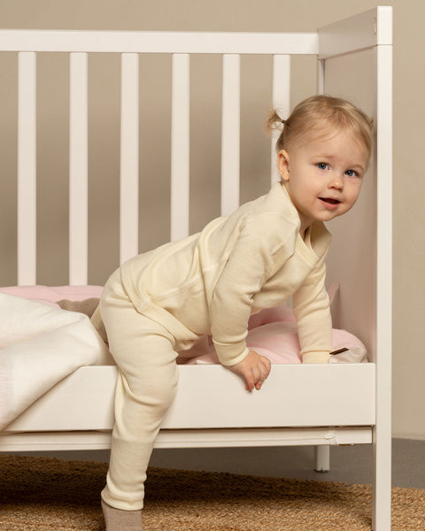 little girl in natural color matching merino thermal set jumping out of the bed