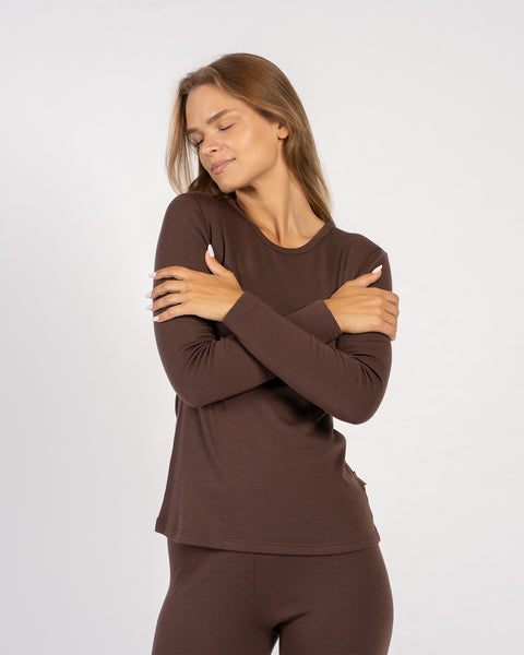 Relaxed pose of woman hugging herself in brown merino wool thermal set.