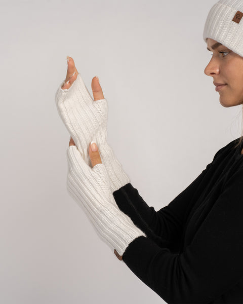 Close-up profile showing beanie label and the ribbed texture of the white fingerless gloves on her hands.