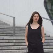 A young girl posing outdoors in a city on a concrete stairs, wearing linen pure black tank top Hana, and pure black pants dakota.