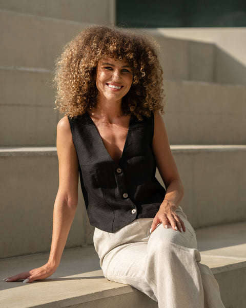 Linen vest ava in black paired with natural color linen pants. Women is sitting and smiling