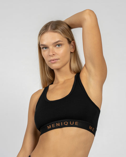 Woman wearing a black Merino wool sports bra with racerback design, posing with one arm raised.