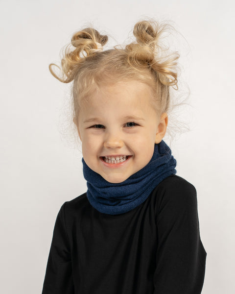 Close-up of a happy child in a black shirt wearing a dark blue knit neck warmer, smiling at the camera.