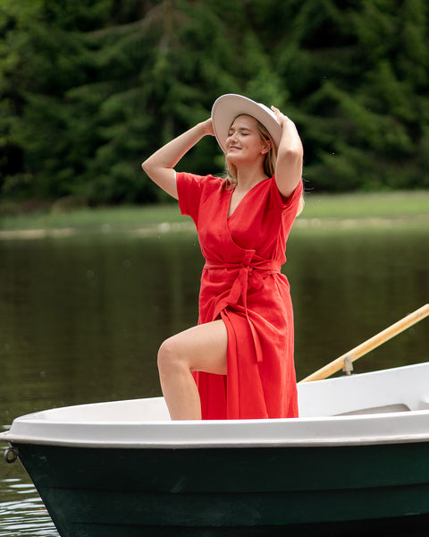 Woman wearing red wrap midi dress sitting in a boat on a lake, lightweight elegant summer outfit