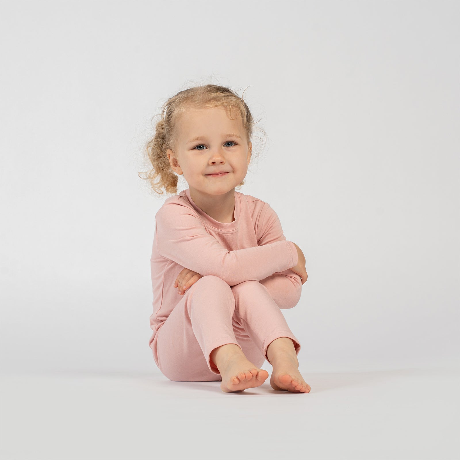 Child wearing pink bamboo long-sleeve top and matching pants, standing barefoot against a plain light background.