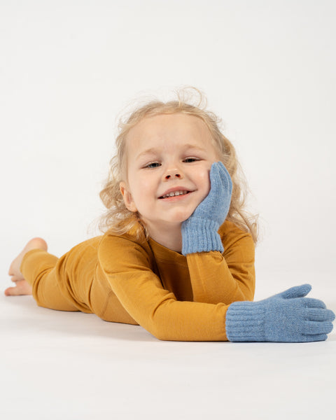 A young child with curly blonde hair and a bright smile wearing light blue gloves on a white background