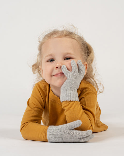 A young child with curly blonde hair wearing light gray gloves on a white background