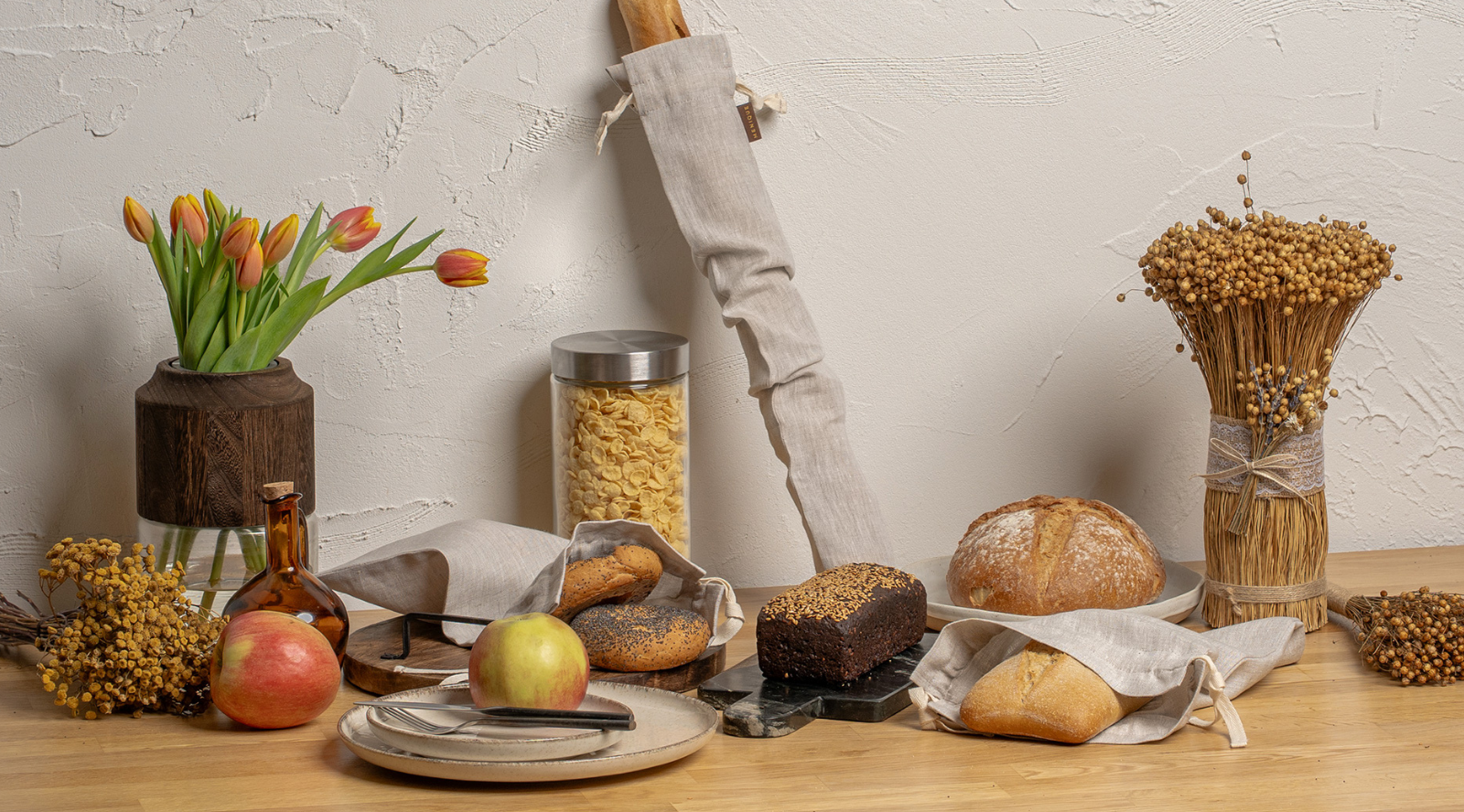 Linen bread bag and fresh baked goods on kitchen counter with apples and glass jar