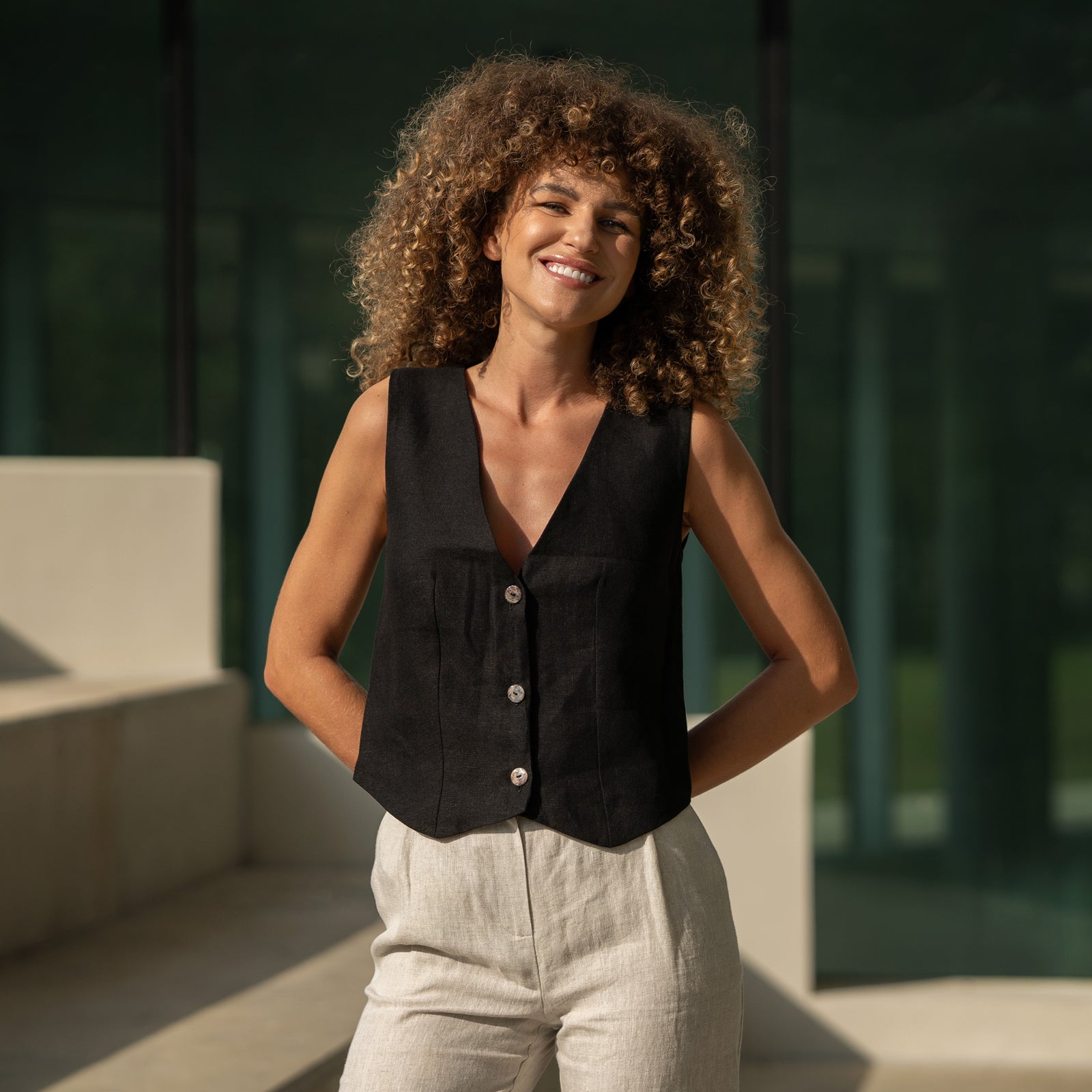 The menique women's linen est AVA in natural color. The woman is holding a metal railing, smiling.