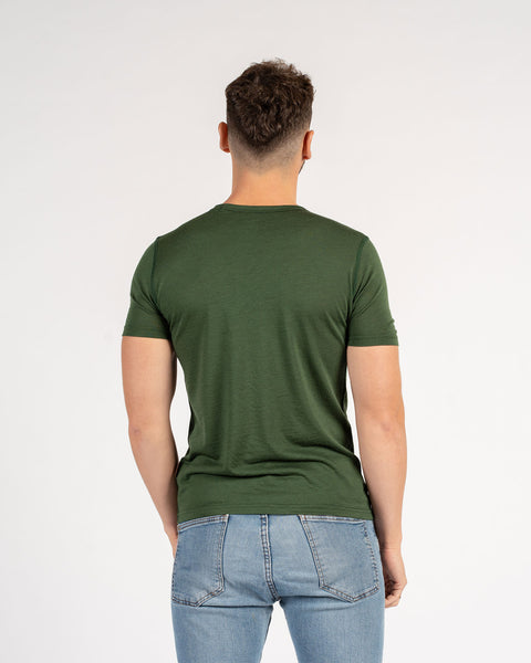 Back view of man in a dark green slim fit Merino wool t-shirt with blue jeans.