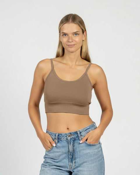 Woman wearing a brown crop top and blue jeans on a plain background