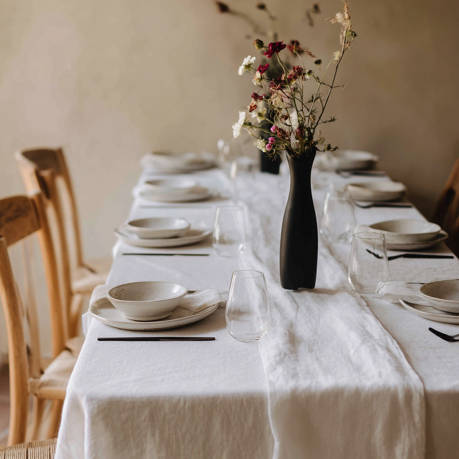 A serene, elegant dining table draped in a crisp, pure white linen tablecloth with a relaxed, textured table runner down the center.
