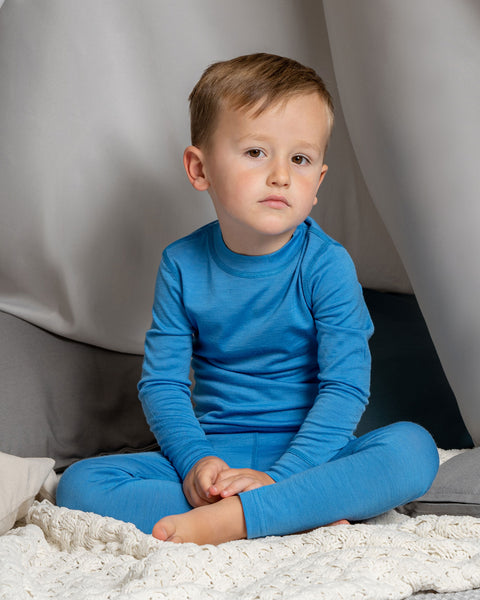 A boy sitting in a indoor play tent, wearing the 160gsm merino long sleeve top in light blue color. 