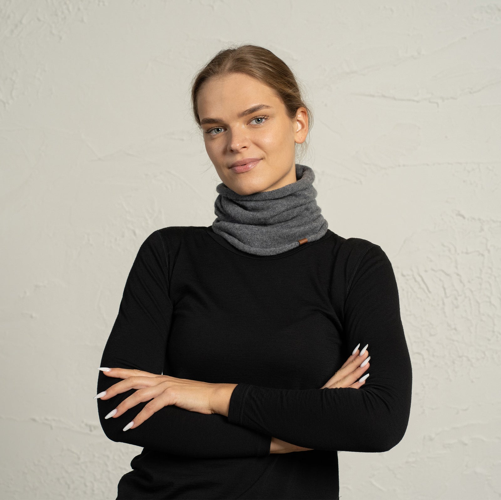 Woman wearing a beige merino wool neck gaiter, standing with arms crossed and looking at the camera.