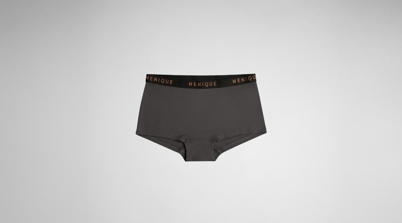 A pair of dark grey boyshort-style underwear featuring a black elastic waistband with the brand name "MENIQUE" written in copper-colored text, centered against a light grey background.