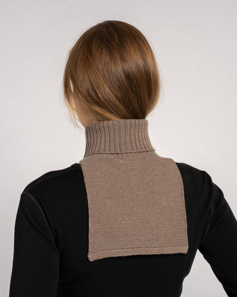 Back view of a woman wearing a brown knitted merino wool dickie neck warmer over a black top.