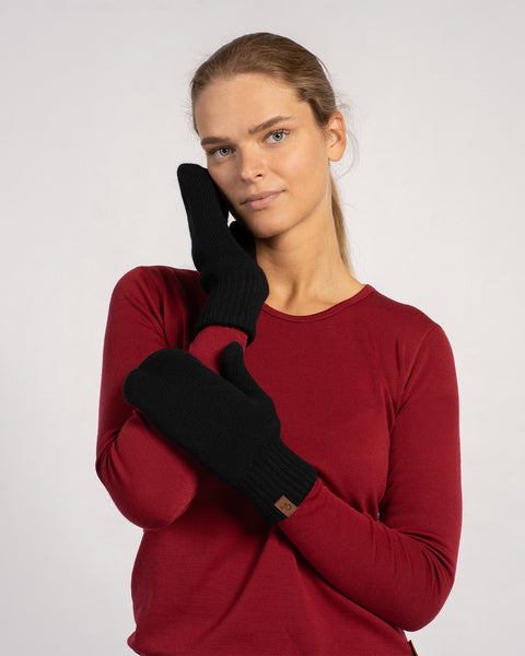 Woman posing in black knitted merino wool mittens with a red long-sleeve top, hand resting on face.