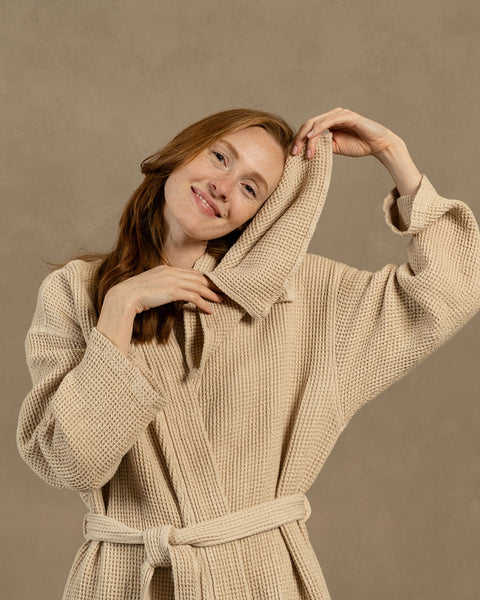 A woman holding a waffle washcloth Face Towel of 30x30cm dimensions by her face, in Sand Brown color.