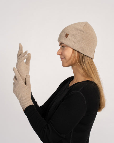 Woman wearing a creamy beige cashmere beanie and matching short gloves, side profile view, adjusting the glove.
