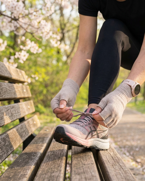 Close-up of woman tying running shoes while wearing beige merino wool fingerless gloves, breathable lightweight running gloves for spring workouts and outdoor training