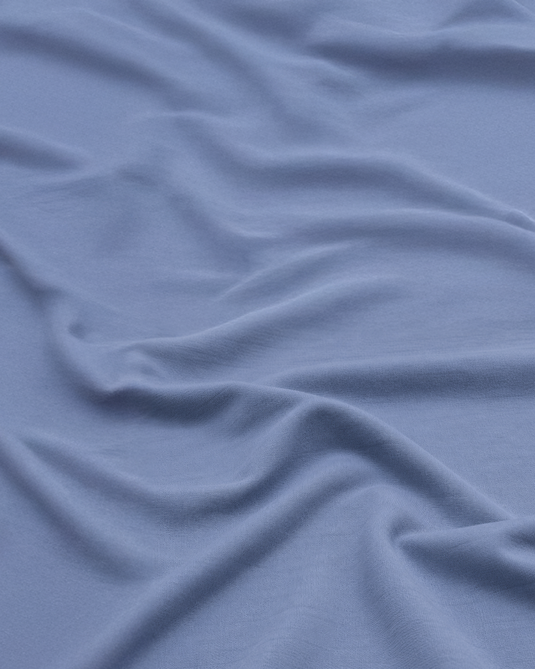 A close-up view of light periwinkle-blue fabric, gently gathered to highlight its soft texture and subtle draping.
