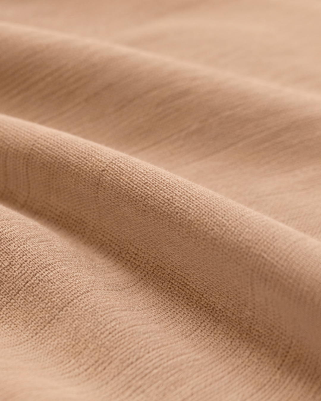 A close-up view of soft, light brown textured fabric draped to create gentle, rolling folds.