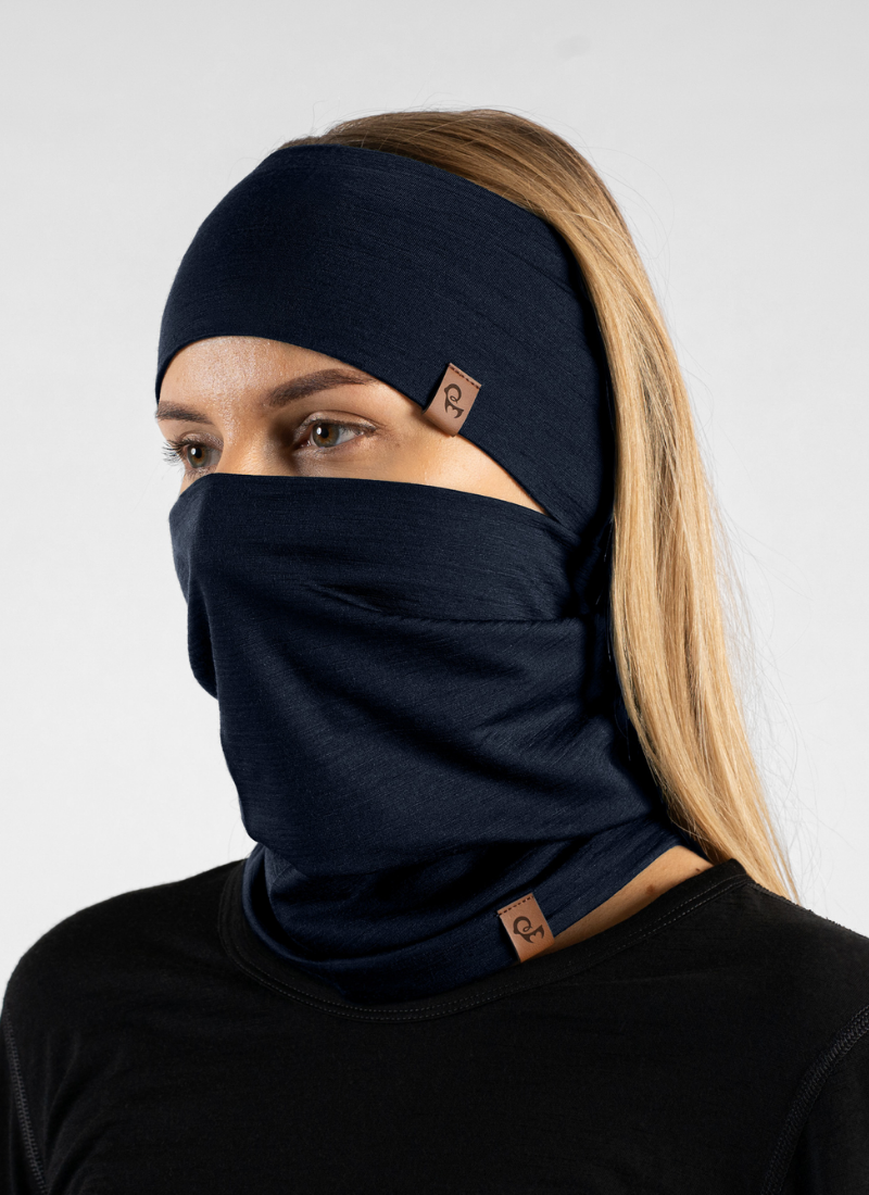 A woman wearing a dark navy blue balaclava face mask and matching headband, shown from the chest up against a light gray studio background.