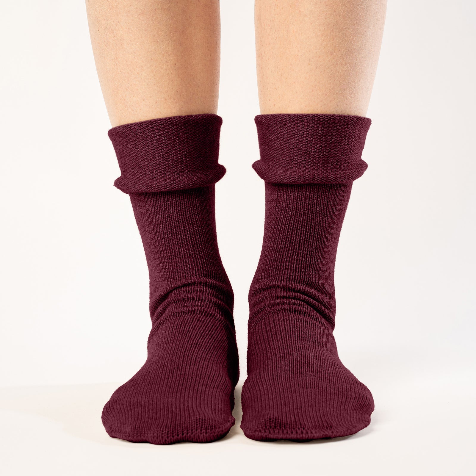 A person is shown from the mid-thigh down, wearing ribbed, royal cherry colos socks. The socks are pulled up to the mid-calf, and the person's feet are slightly apart against a plain white background. The lighting is even, highlighting the texture of the socks.