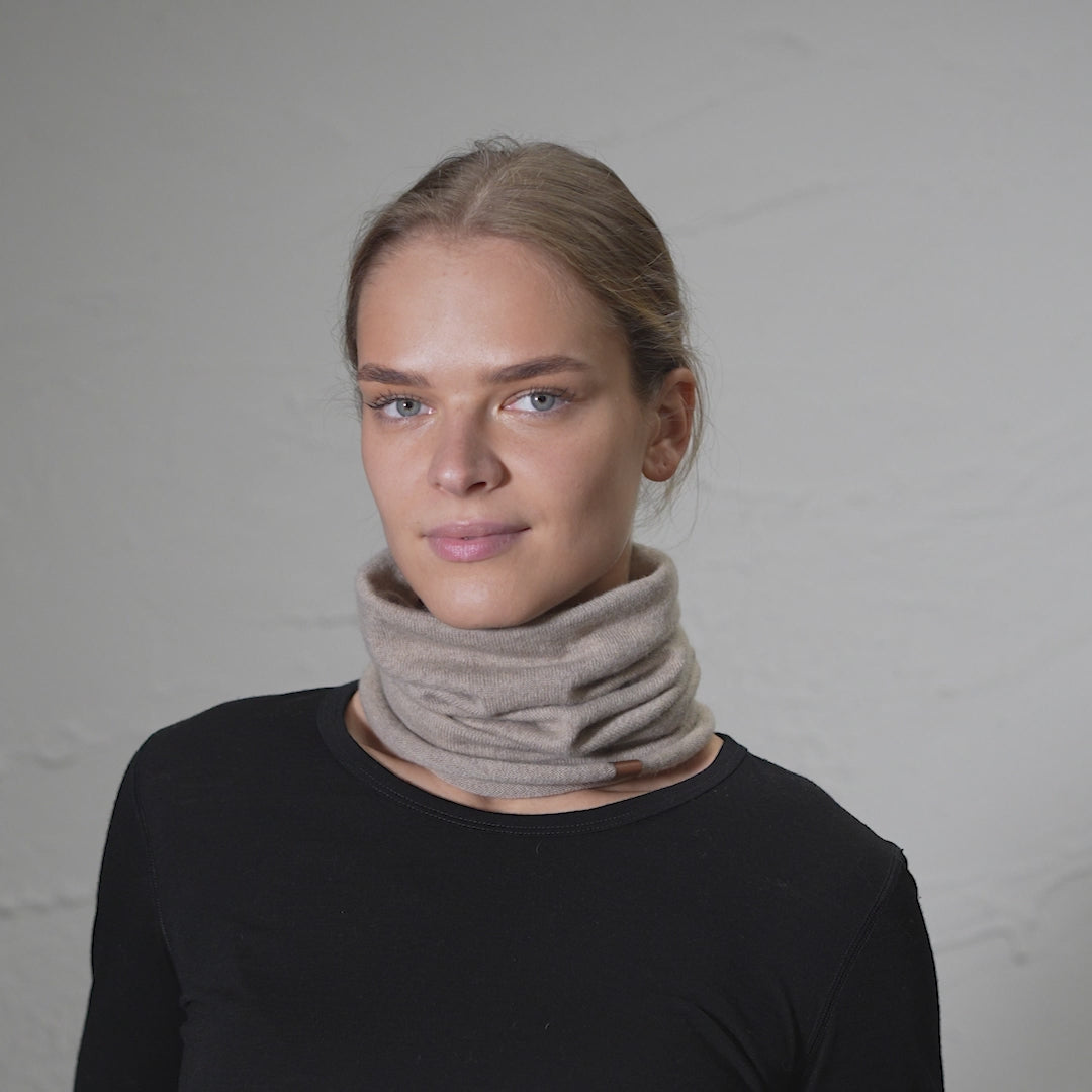 Model wearing merino wool & cashmere snood gaiter, turning slightly and looking to the side in a studio setting.