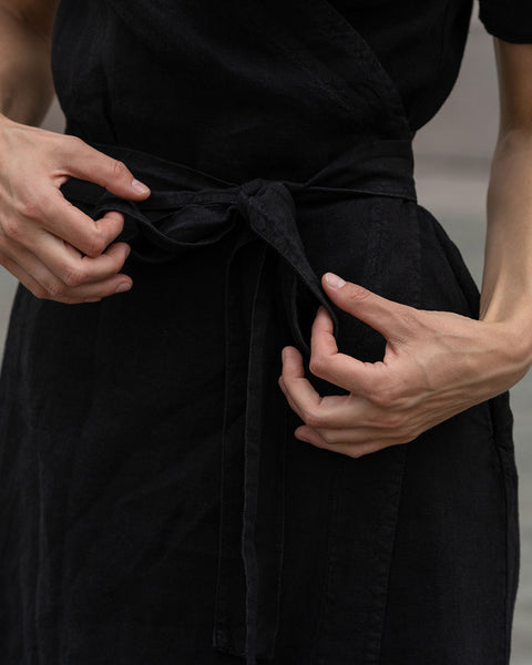 Close-up of a woman tying up a belt on a pure black linen dress Eliana.