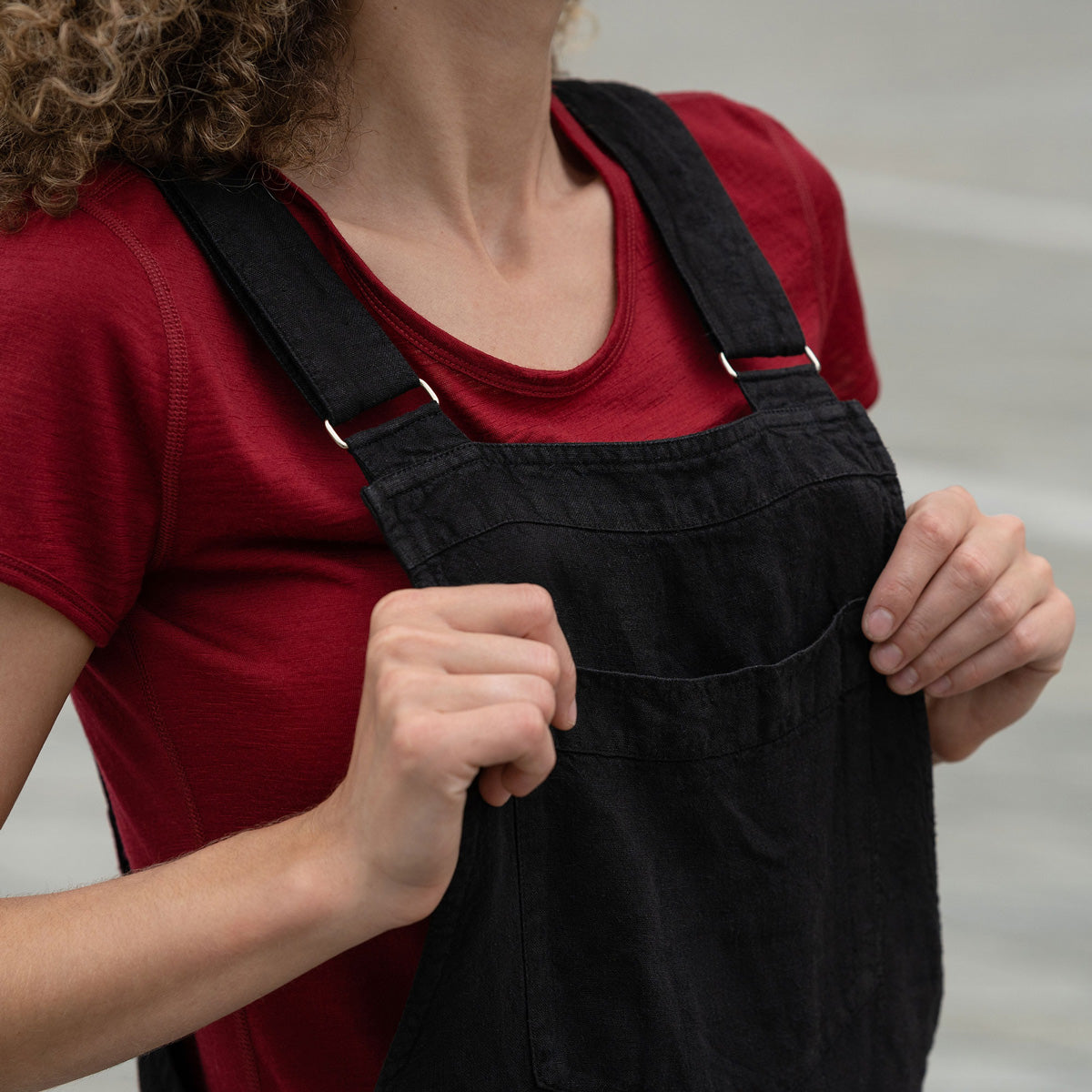 Beautiful woman with curly hair posing in the city wearing pure black linen jumpsuit Nicci, royal cherry merino wool top. Posing with a brown poodle dog.