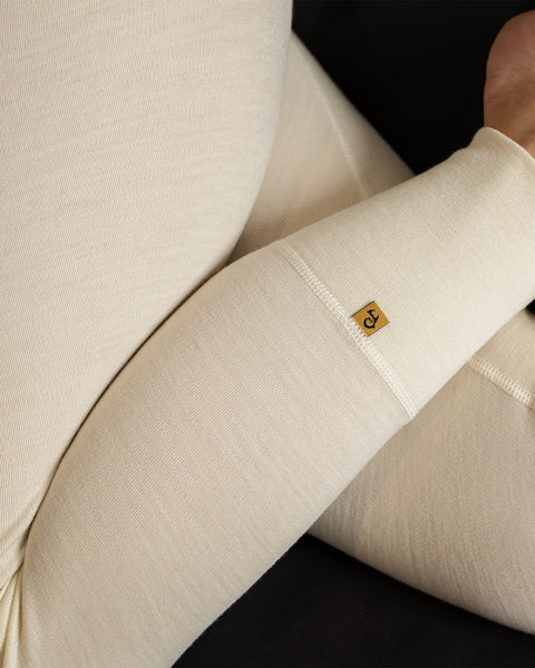 A close-up of a pair of natural-colored leggings made of merino wool is shown. The leggings have a high waist and a form-fitting silhouette. The fabric has a smooth, matte finish and is free of any visible embellishments or patterns.
